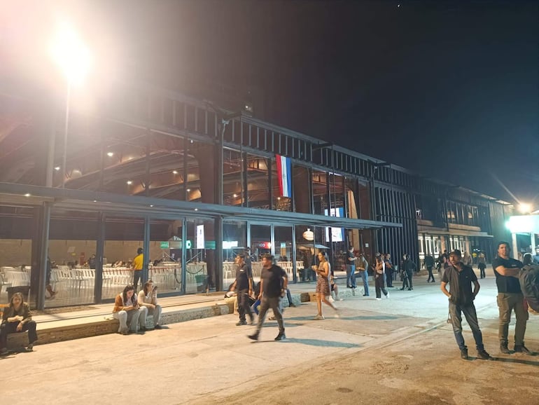 Gente en un ambiente moderno y iluminado, algunas observando sus teléfonos, con mesas y sillas visibles.