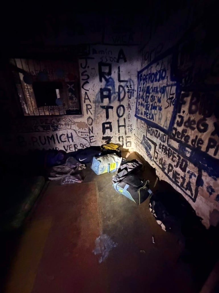 Espacio interior con mochilas desordenadas y paredes cubiertas de grafitis, sin personas visibles en la imagen.