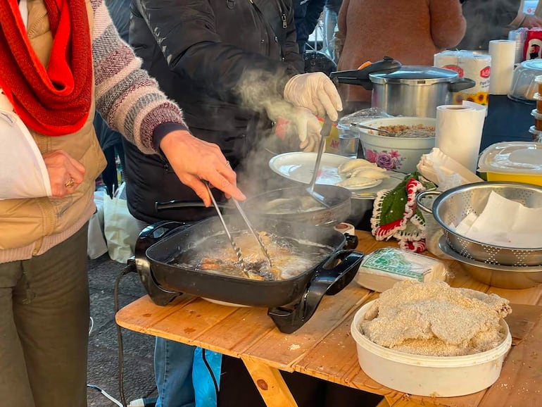 Mujeres en bufanda roja y guantes, cocinando alimentos en una mesa de madera en un ambiente al aire libre.