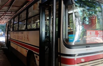 Autobús de transporte público de colores blanco y rojo, estacionado en un área cubierta con luz natural.