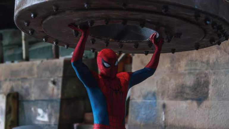Personaje con traje rojo y azul de Spider-Man levanta una estructura metálica en un espacio industrial vacío.