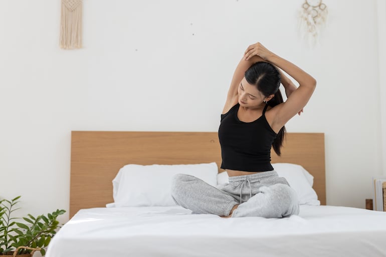 Mujer hace su rutina de estiramientos en la cama.