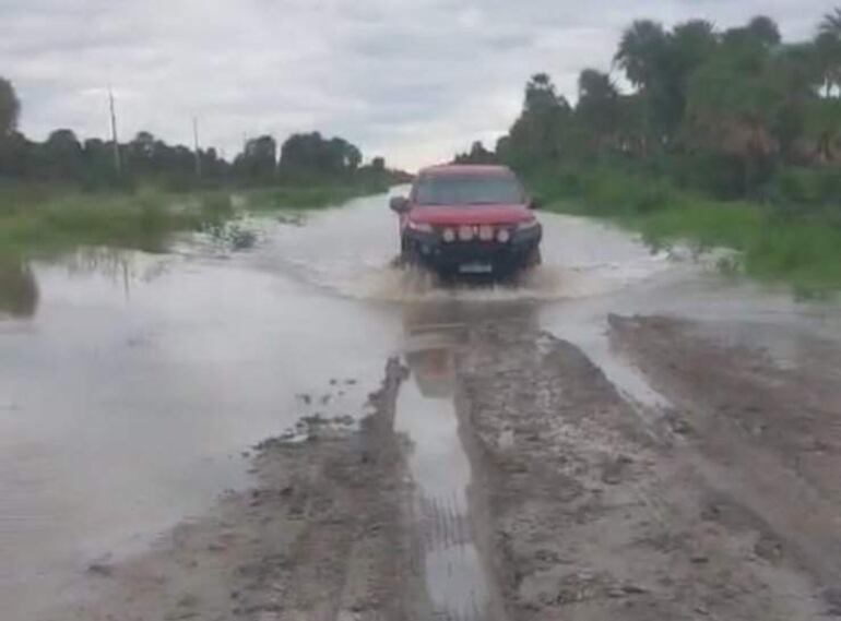 Camioneta roja surca un camino anegado, salpicando agua bajo un cielo nublado y rodeada de vegetación.