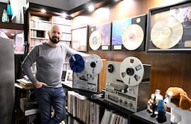 Jorge Puig con suéter gris y jeans, sonriendo y apoyado en un equipo de audio vintage en un estudio musical.