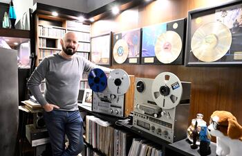 Jorge Puig con suéter gris y jeans, sonriendo y apoyado en un equipo de audio vintage en un estudio musical.