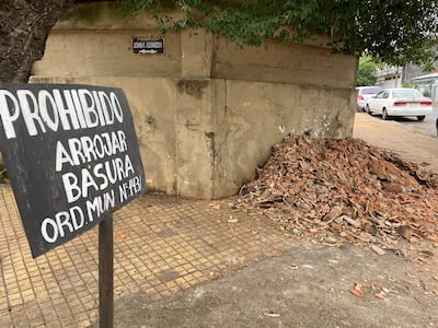 Letrero negro con letras blancas que indica 'PROHIBIDO ARROJAR BASURA' junto a escombros en un sendero urbano.