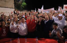 Grupo de personas levantando dos dedos en señal de victoria, vestimenta blanca y roja, sonrisas y ambiente festivo al aire libre.