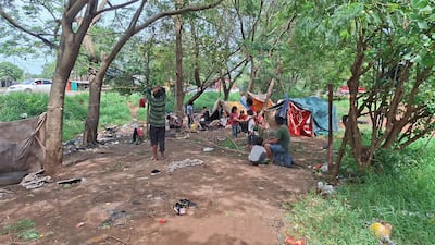 Grupo de personas indígenas en carpas improvisadas, con signos de preocupación y niños en el suelo, rodeados de árboles.