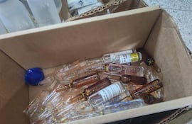 Caja de cartón repleta de ampollas y frascos vacíos en un entorno clínico, sin personas visibles.