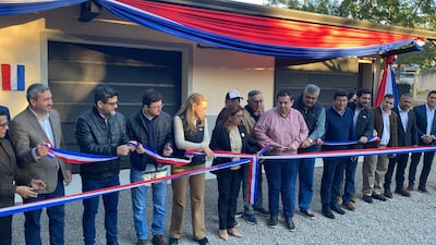Arturo Urbieta y María Teresa Barán sostienen un listón tricolor en un evento público, rodeados de personas atentas y un ambiente festivo.