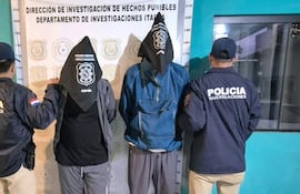 Cuatro hombres en chaquetas: tres con bolsas en la cabeza; un oficial de policía reconoce su uniforme en un ambiente interior.