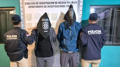 Cuatro hombres en chaquetas: tres con bolsas en la cabeza; un oficial de policía reconoce su uniforme en un ambiente interior.