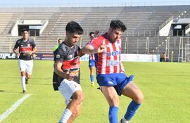 El atacante de Encarnación, Fernando Escobar intenta proteger la posesión del esférico ante la marca del lateral del Kelito, Damián Cabrera. (Foto: @IntermediaAPF)
