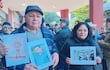 Hombre y mujer sostienen carteles con fotos, rodeados de un grupo de personas vistiendo abrigos en un acto de memoria histórica.