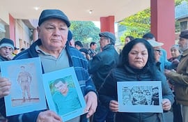 Hombre y mujer sostienen carteles con fotos, rodeados de un grupo de personas vistiendo abrigos en un acto de memoria histórica.