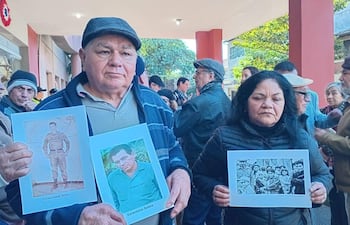 Hombre y mujer sostienen carteles con fotos, rodeados de un grupo de personas vistiendo abrigos en un acto de memoria histórica.