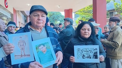 Hombre y mujer sostienen carteles con fotos, rodeados de un grupo de personas vistiendo abrigos en un acto de memoria histórica.