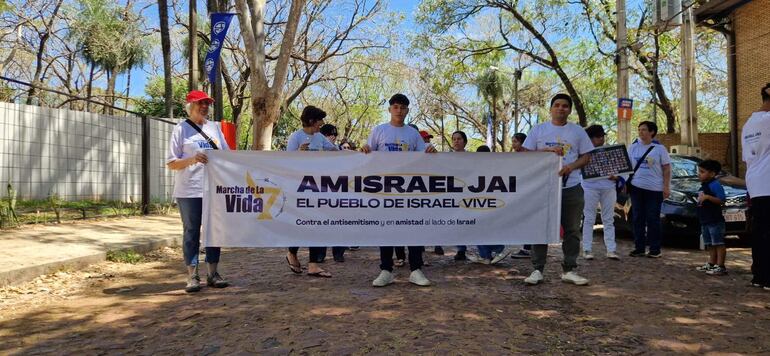 Seis personas con camisetas blancas sosteniendo un banner, una gorra roja visible, en un entorno de manifestación pacífica.