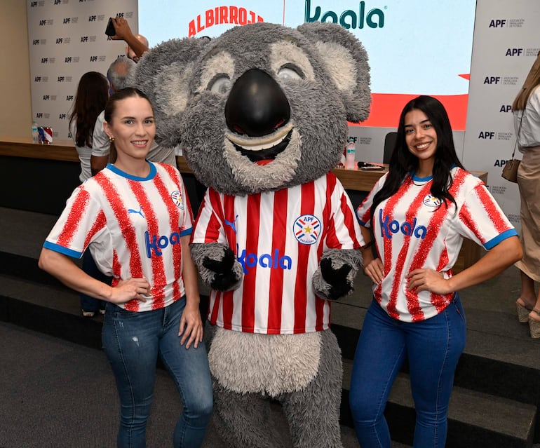 Mujer con vestimenta de selección paraguaya y hombre con chaqueta azul en evento formal de Koala y la APF, con logo de Albirroja visible.