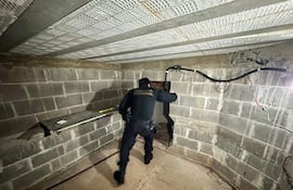 Agente en uniforme oscuro de Policía Federal revisa habitación con luces tenues y objetos en el suelo.
