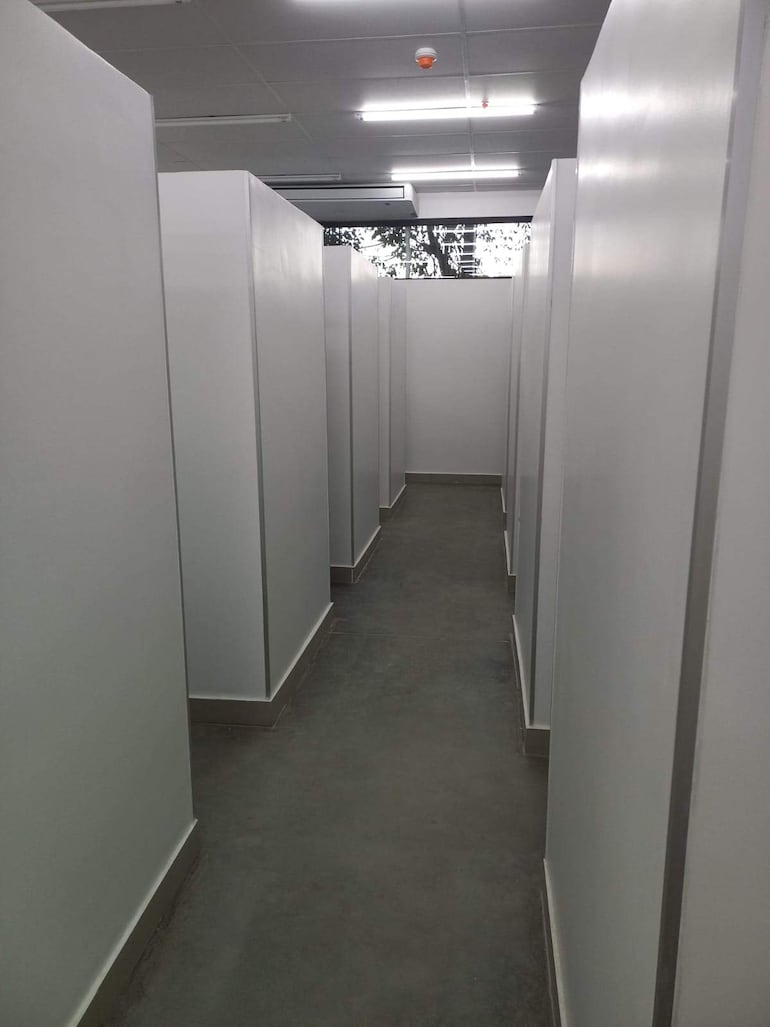 Pasillo interior limpio y ordenado, con divisiones blancas y suelo de concreto, sin personas presentes.