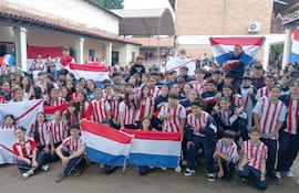 Estudiantes en camisetas rojas y blancas ondean banderas de Paraguay, mostrando alegría y unidad.