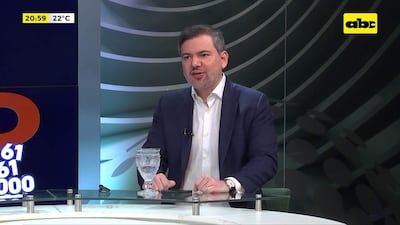 José Duarte Penayo, con saco oscuro y camisa blanca, habla en un set de televisión con fondo verde y elementos de cristal.
