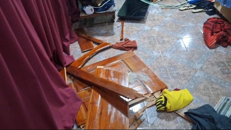 Ambiente interior desordenado con piezas de madera y ropa de colores, sugiere un evento reciente brusco.