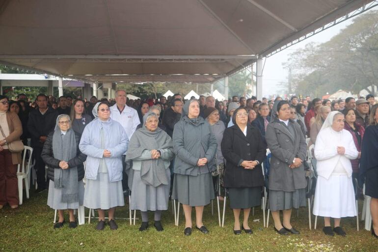 Grupo de mujeres con hábitos religiosos en actitud de oración, rodeadas de una multitud en un evento al aire libre.