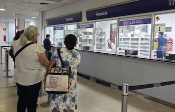 Mujeres en la fila de la farmacia. Una usa lentes y la otra lleva un vestido floral y mochila con diseño de búhos.
