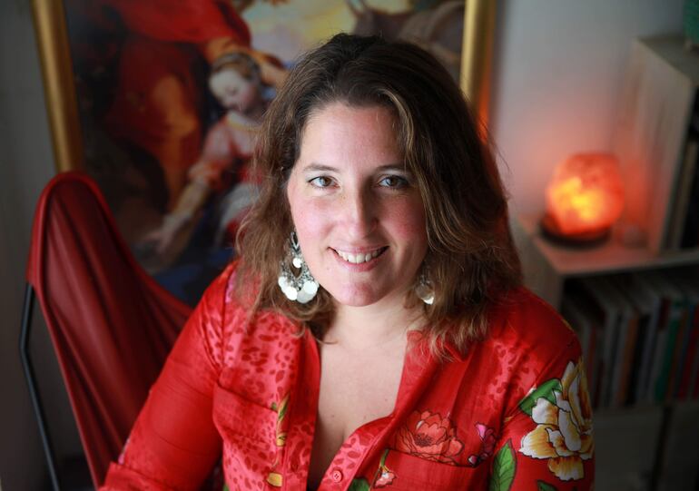 Agustina Bazterrica luciendo blusa roja con flores y sonriendo en ambiente cálido, rodeada de libros y arte.