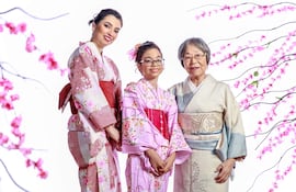 Mujer con kimono rojo, niña en kimono rosa y mujer mayor en kimono gris claro, sonriendo en un entorno festivo con flores de cerezo.