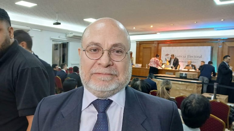 Luis Fretes Carreras, con camisa blanca y saco gris, escucha atentamente en una sala con un cartel de Justicia Electoral.