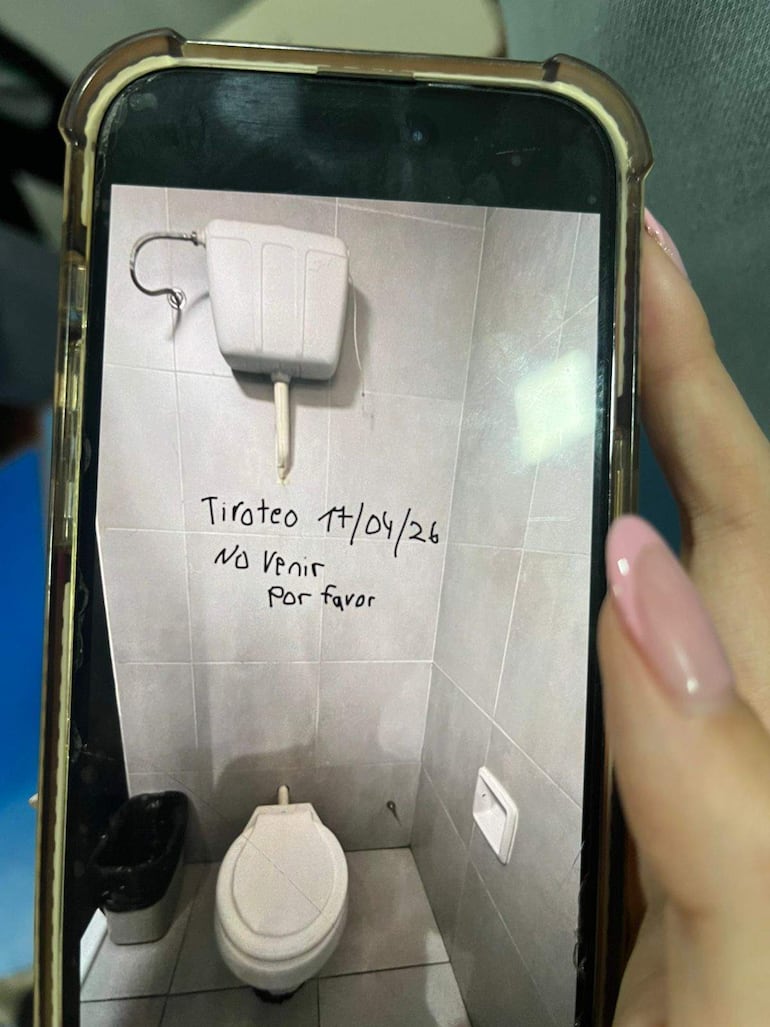 Un baño con un inodoro y papelera negra. En la pared se lee un mensaje alarmante sobre un tiroteo.