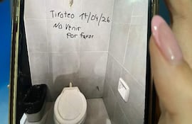 Un baño con un inodoro y papelera negra. En la pared se lee un mensaje alarmante sobre un tiroteo.