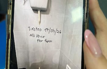 Un baño con un inodoro y papelera negra. En la pared se lee un mensaje alarmante sobre un tiroteo.