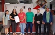 Mujer en blusa negra sostiene un documento mientras hombres la observan en oficina con mobiliario visible.