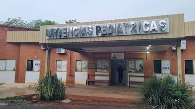 Entrada de urgencias pediátricas con cartel metálico, plantas decorativas y un pasillo que conduce al interior.