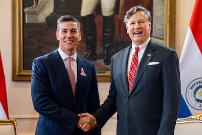 Santiago Peña, en traje oscuro y corbata a rayas, sonríe mientras saluda a Christopher Landau, que lleva un traje oscuro y corbata rosa.