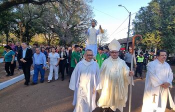Dos sacerdotes en vestimenta blanca y dorada lideran una multitud en procesión, mientras otros asistentes con ropa formal los acompañan.