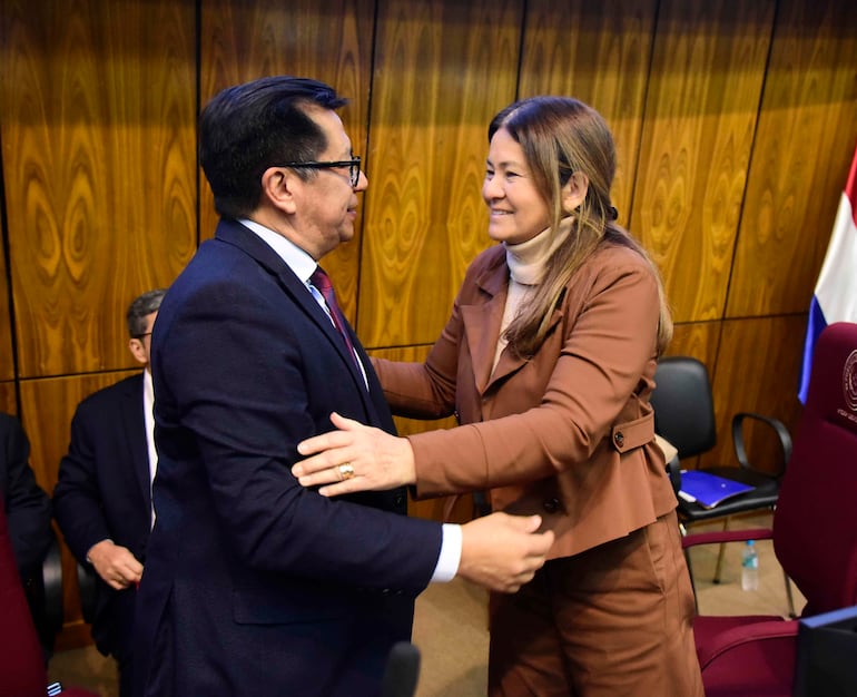 Tadeo Rojas en traje oscuro y corbata, sonriente, junto a Cristina Villalba, con cabello largo y conjunto marrón, en un entorno oficial.