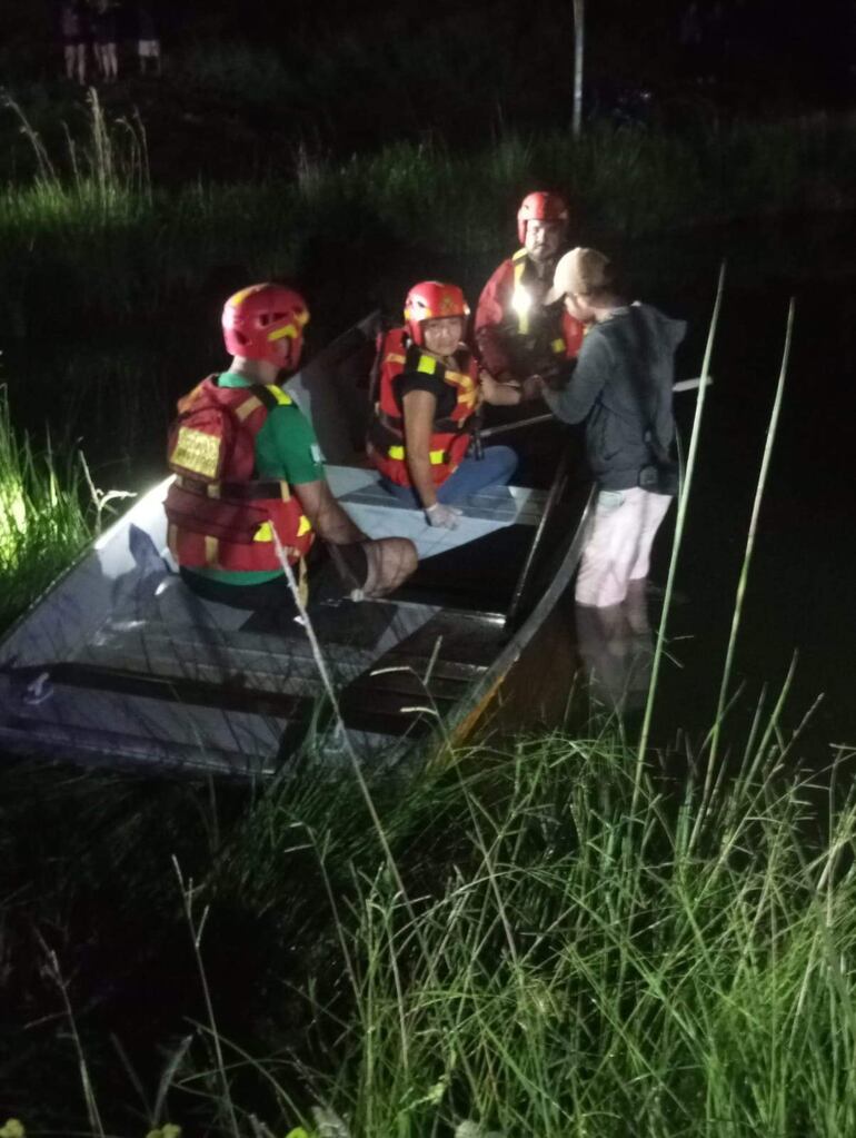 Cuatro rescatistas en chalecos salvavidas en lancha, concentrados mientras se desarrollan las labores de búsqueda en la oscuridad.