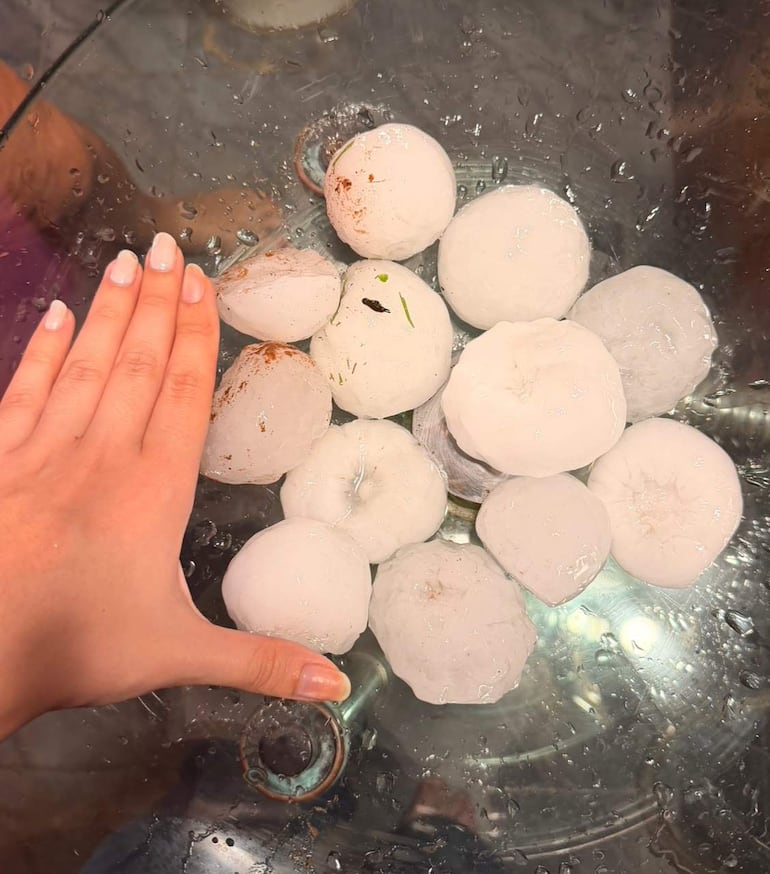 Bolas de hielo de gran tamaño sobre una superficie de vidrio, con una mano al lado, rodeadas de agua derretida.