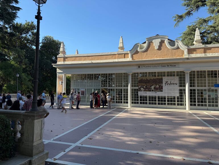Multitud en fila en el Centro Cultural Casa de Vacas, con árboles al fondo y un cartel sobre la antológica de Antonio Pedrero.