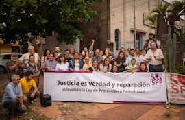 Grupo de personas aplauden con pancarta pidiendo justicia y protección a periodistas en un ambiente sereno.