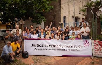 Grupo de personas aplauden con pancarta pidiendo justicia y protección a periodistas en un ambiente sereno.