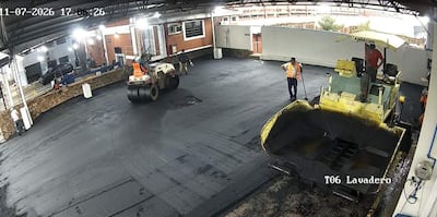 Cinco trabajadores en ropa de alta visibilidad, uno en rodillo compactador y otros supervisando en ambiente iluminado.