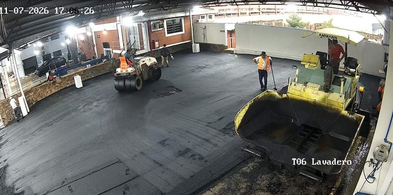 Cinco trabajadores en ropa de alta visibilidad, uno en rodillo compactador y otros supervisando en ambiente iluminado.