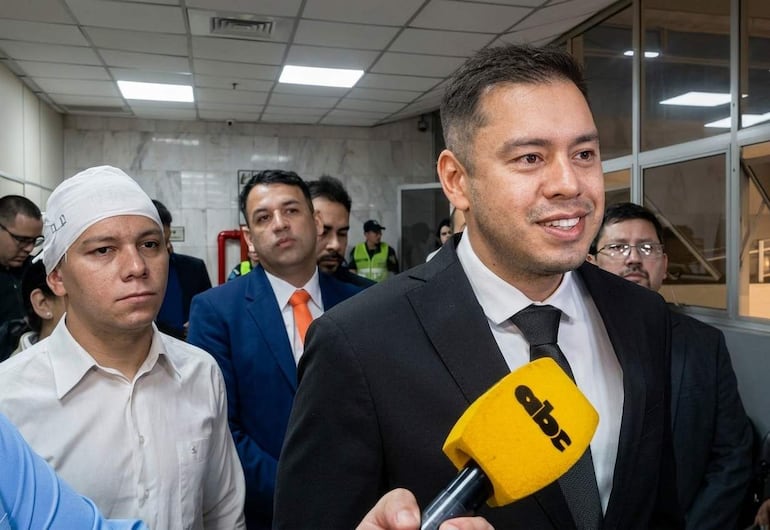 Bruno Martínez, con venda en la cabeza, y Miguel Prieto, en traje oscuro, se dirigen a la prensa en un ambiente formal.