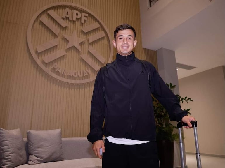 Andrés Cubas sonriente en chaqueta negra, sosteniendo una maleta, con el logo de la APF de fondo.